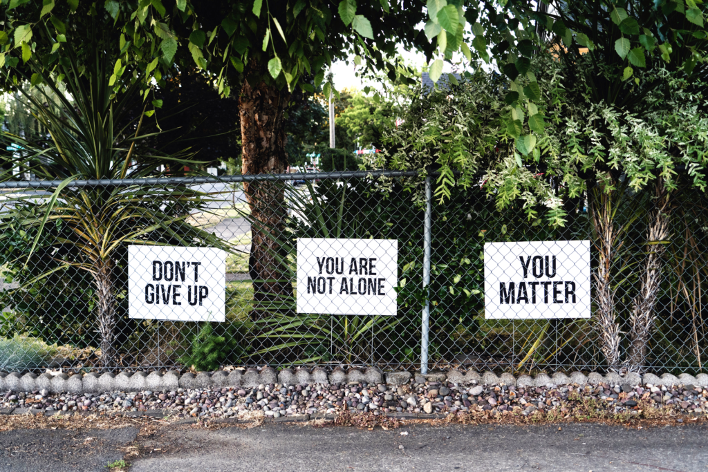 Signs on a chain link fence saying don't give up, you are not alone, you matter