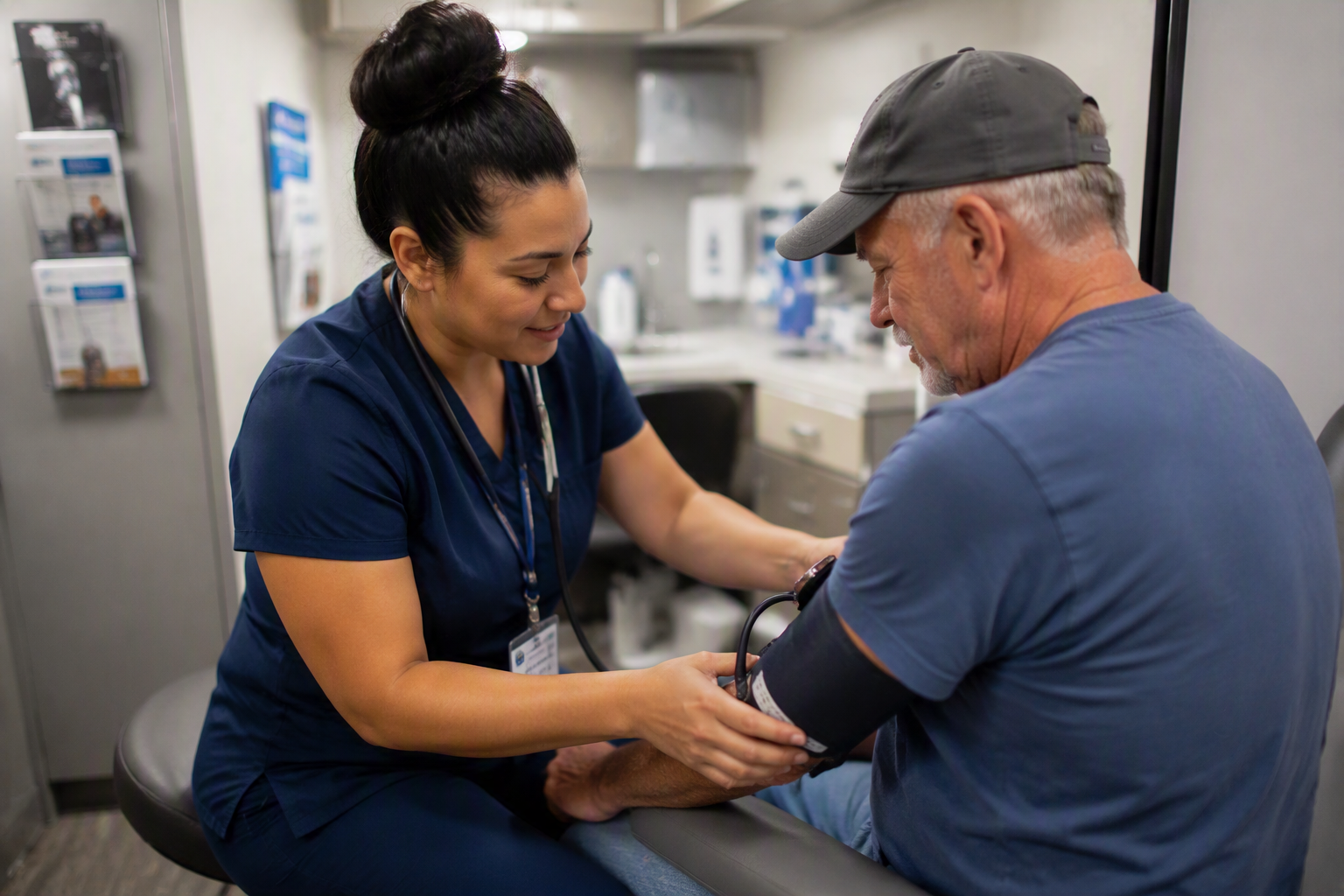 Healthcare provider checking a patient's blood pressure during a visit inside a mobile health clinic exam room.